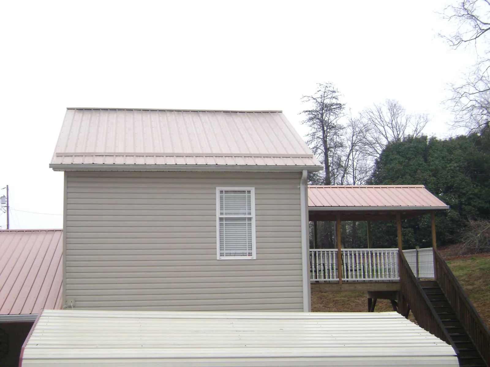 Tan metal roofs on a two story addition and attached porch, from a Roof Replacement job in Russellville